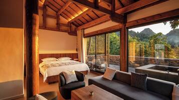 A bedroom with a large bed, a sofa, and a coffee table. There is a view of a mountainous landscape through large windows.