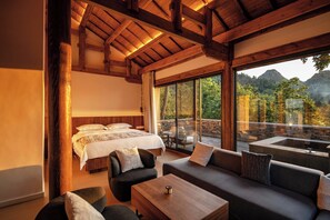 A bedroom with a large bed, a sofa, and a coffee table. There is a view of a mountainous landscape through large windows. - Zhiye Resort Hotel (Anshun)