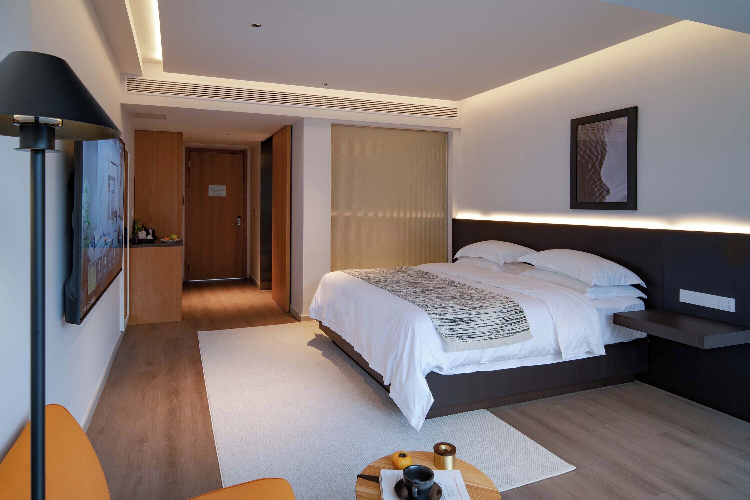 Ein modernes Hotelzimmer mit Bett, Nachttisch, Lampe und Kunstwerk.