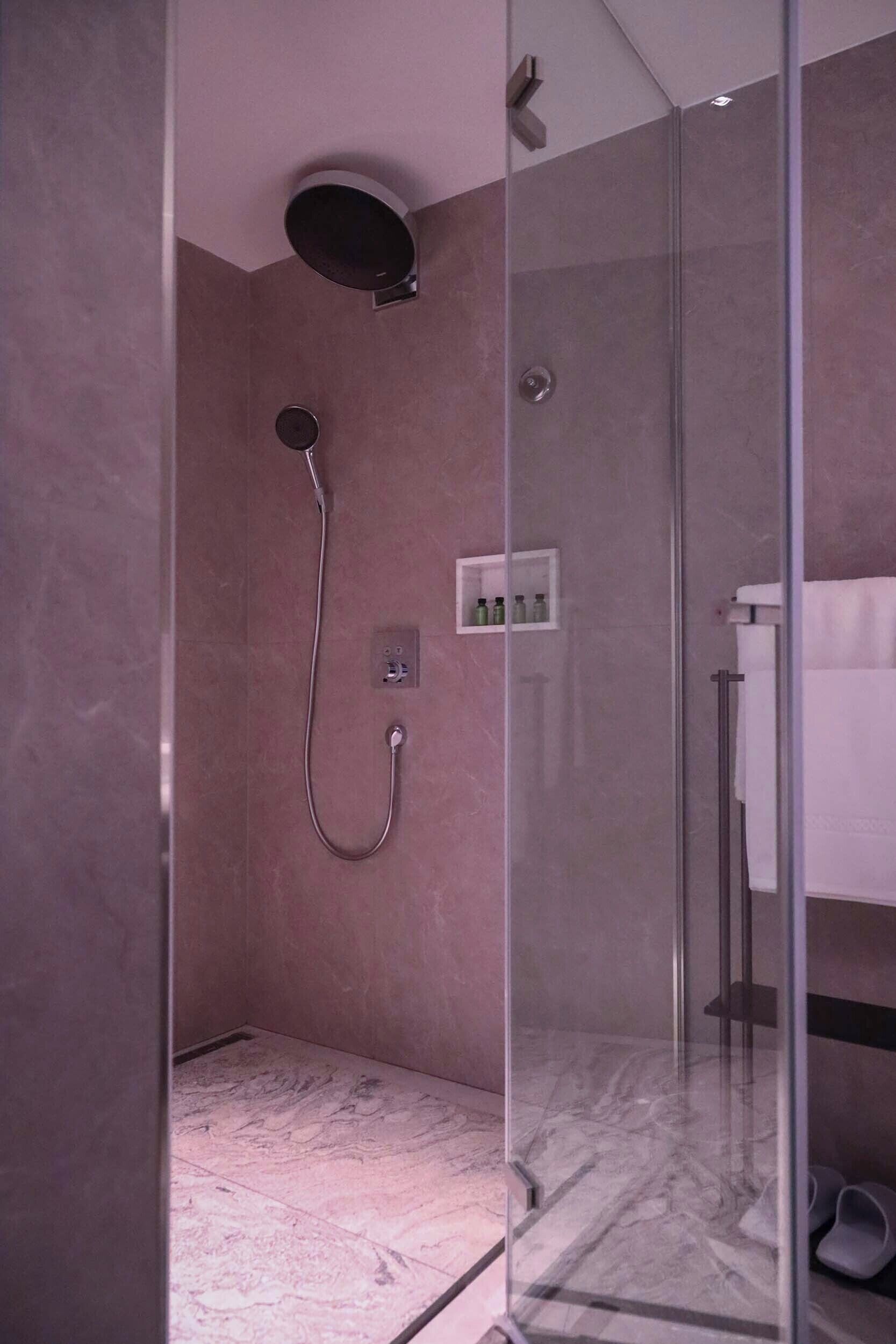 A modern bathroom with a glass-enclosed shower, a marble floor, and a white towel rack.