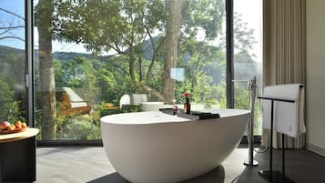 Un baño moderno con una bañera grande, un perchero y vistas a un bosque a través de amplios ventanales.