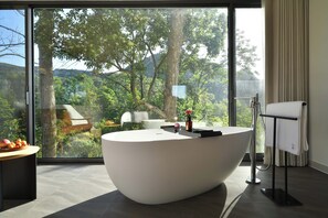 A modern bathroom with a large bathtub, a towel rack, and a view of a forest through large windows. - Zhiye Resort Hotel (Anshun)