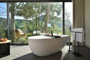 Un baño moderno con una bañera grande, un perchero y vistas a un bosque a través de amplios ventanales.