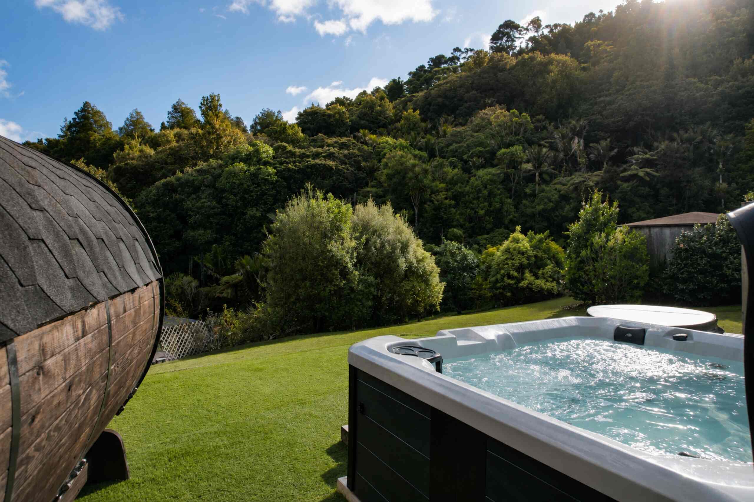 Un jacuzzi en un patio trasero con una estructura de madera y abundante vegetación al fondo.