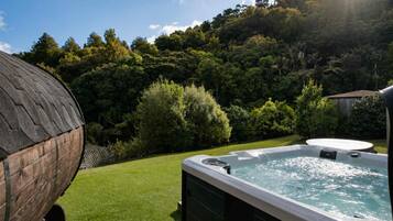 Un jacuzzi en un patio trasero con una estructura de madera y abundante vegetación al fondo.