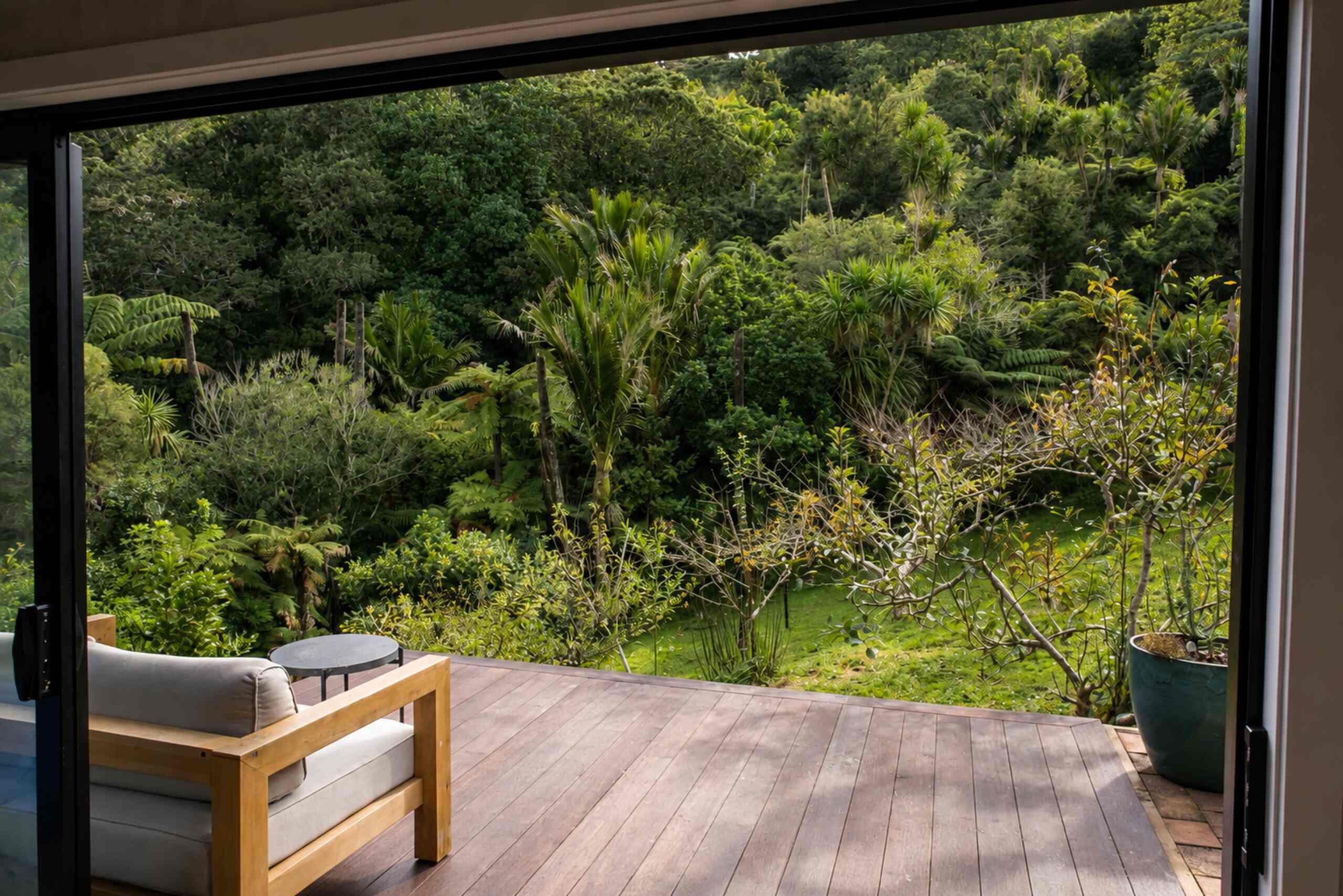 A wooden deck with a bench and a table, overlooking a lush garden with various plants and trees.
