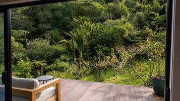 A wooden deck with a bench and a table, overlooking a lush garden with various plants and trees.