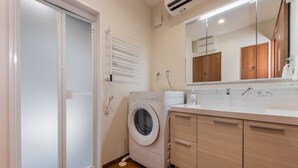 A modern bathroom with a built-in washing machine, a mirror, and wooden cabinets. - Kikou (Kyoto)