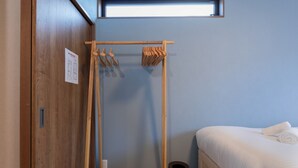 A small, compact room with a wooden wardrobe, a bed with white bedding, a small window, and a towel rack. - Kikou (Kyoto)