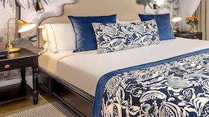 Habitación de hotel con una cama, una mesita de noche, una lámpara, un ventilador de techo y un mural tropical en la pared.