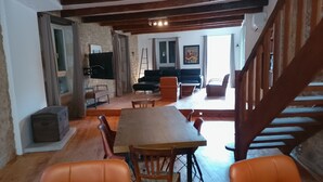 Un vaste espace de vie comprenant une table à manger en bois, des chaises orange, un canapé noir et un escalier menant à un niveau supérieur.