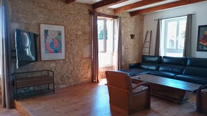 Une pièce avec un mur en pierre, des poutres apparentes, un canapé en cuir, une table basse en bois et un téléviseur.