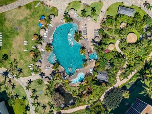 An aerial view of a resort with a central swimming pool, sun loungers, palm trees, and a small waterfall. - Large 1BR condo, partial ocean view, pool, beach access - Kaanapali Shores 414 (Lahaina)