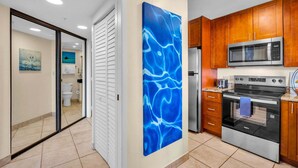 Une cuisine moderne avec des meubles en bois, des appareils électroménagers en acier inoxydable et une œuvre d’art abstraite bleue au mur.