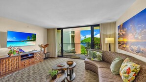 Une chambre d’hôtel avec un balcon, un canapé, une télévision et une armoire en bois.
