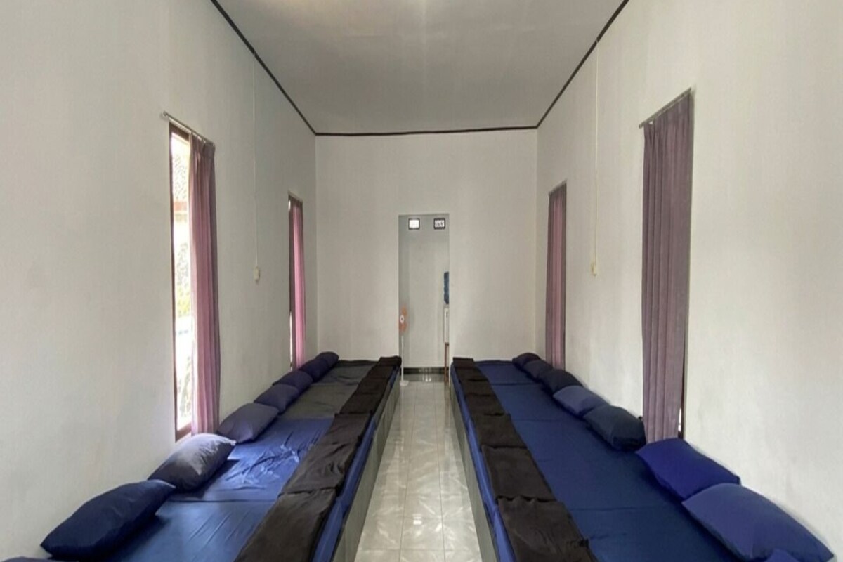 Ein Zimmer mit zwei Reihen von Betten, jeweils mit blauer und schwarzer Bettwäsche, und einem gefliesten Boden.