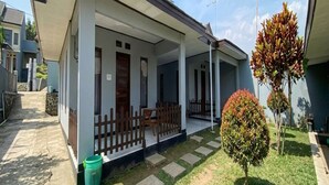 Ein Wohnhaus mit überdachter Veranda, einem kleinen Garten mit Strauch und einem befestigten Auffahrt.
