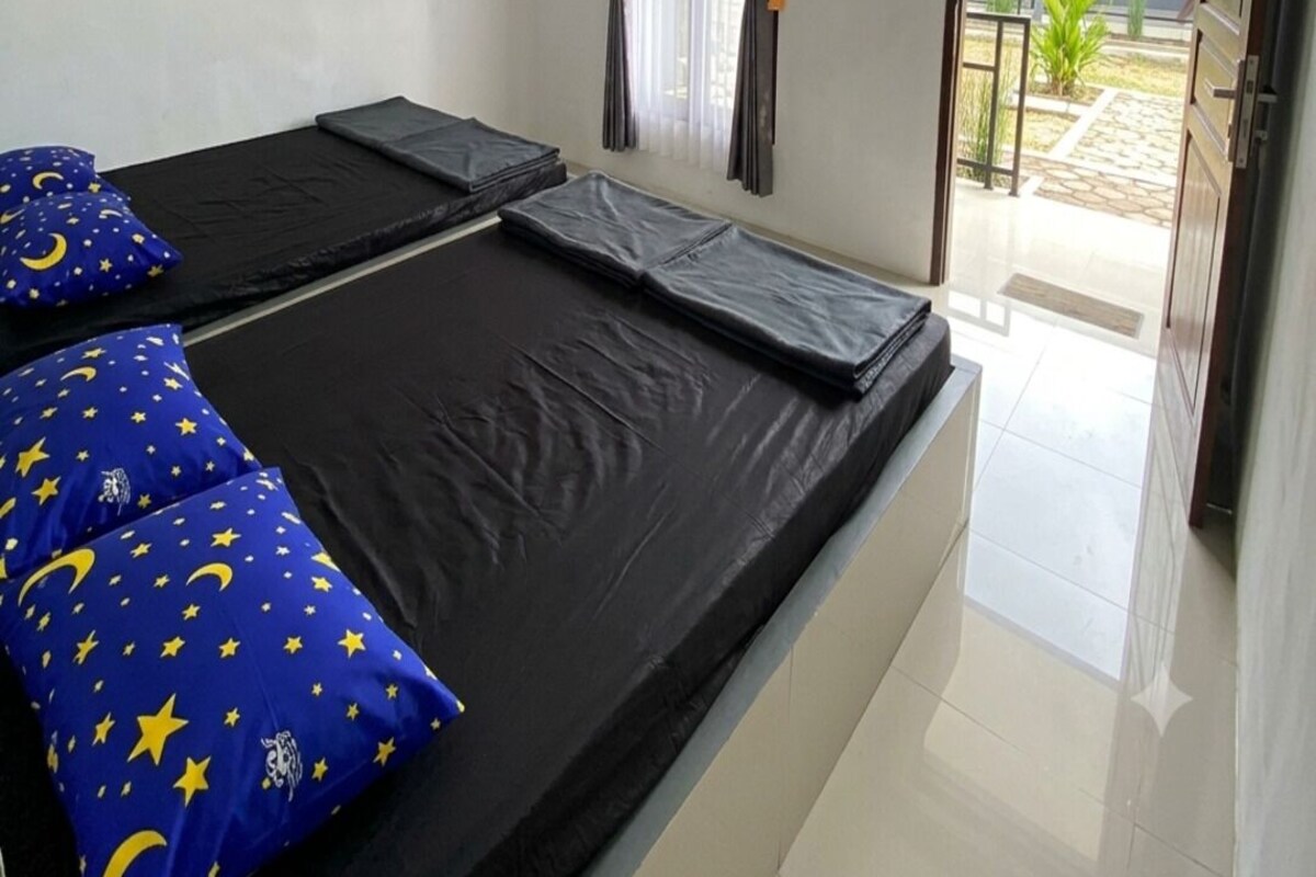 Ein Zimmer mit zwei Betten, einem an der Wand befestigten Fernseher und einer Tür zu einem Außenbereich.