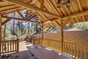 A covered outdoor area with a picnic table, wooden railings, and a view of a forested hillside. - Mountain Air & Game Nights: Pine Mtn Club Cabin (Pine Mountain Club)
