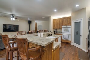 Une cuisine spacieuse avec des meubles en bois, un grand îlot central doté de tabourets, un four encastré et un ventilateur de plafond.