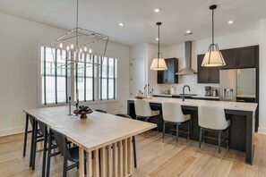 Uma cozinha moderna com ilha central, iluminação pendente e vista para o exterior através de grandes janelas.