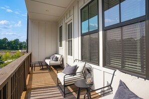 Uma varanda com guarda-corpo de madeira, duas cadeiras de metal com almofadas, uma mesa pequena e vista para o exterior.