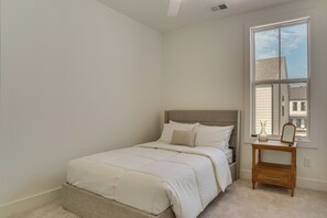 Quarto com cama, mesa de cabeceira, espelho e janela com vista para edifícios.