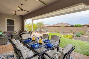 An outdoor patio with a table set for dining, surrounded by chairs, and a ceiling fan above.