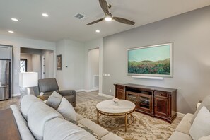 A living room with a ceiling fan, a large painting, a sofa, a coffee table, and a cabinet. - Elegant Home w/ Various Resort Perks in Peoria! (Peoria)