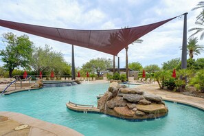 Un área de piscina con toldo sombreado, sillas de descanso y una cascada.
