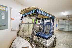 A golf cart with a canopy, located in a garage with a concrete floor and a garage door in the background. - Community Pools, Golf & More! Home in The Villages (The Villages)