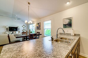 A modern kitchen with granite countertops, stainless steel appliances, and a dining area with a wooden table and chairs. - Community Pools, Golf & More! Home in The Villages (The Villages)