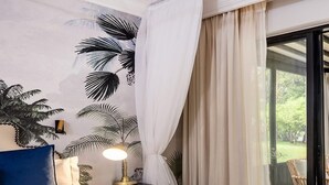 Een slaapkamer met een bed, nachtkastje, lamp en uitzicht op de omgeving door een glazen deur.
