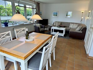 Ein Essbereich mit einem Holztisch und Stühlen, einer Couch und einem Fernseher im Hintergrund.