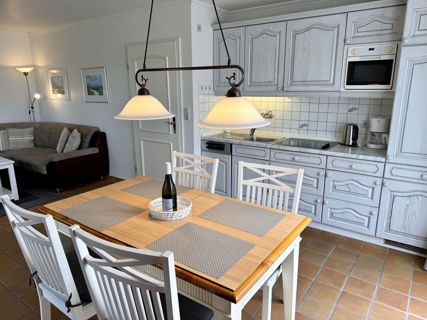 Uma sala de jantar com mesa de madeira, cadeiras brancas e uma garrafa de vinho.