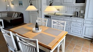 A dining area with a wooden table, white chairs, and a bottle of wine. - Kampstraße, Apartment 2a - Cozy 2-room vacation apartment with a terrace in a quiet (Sylt)