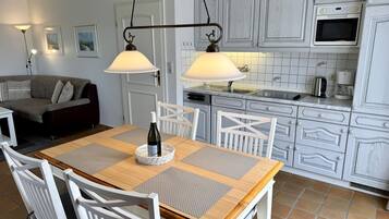 Uma sala de jantar com mesa de madeira, cadeiras brancas e uma garrafa de vinho.