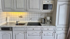 A kitchen with white cabinetry, a built-in oven, a coffee maker, and a dishwasher. - Kampstraße, Apartment 2a - Cozy 2-room vacation apartment with a terrace in a quiet (Sylt)