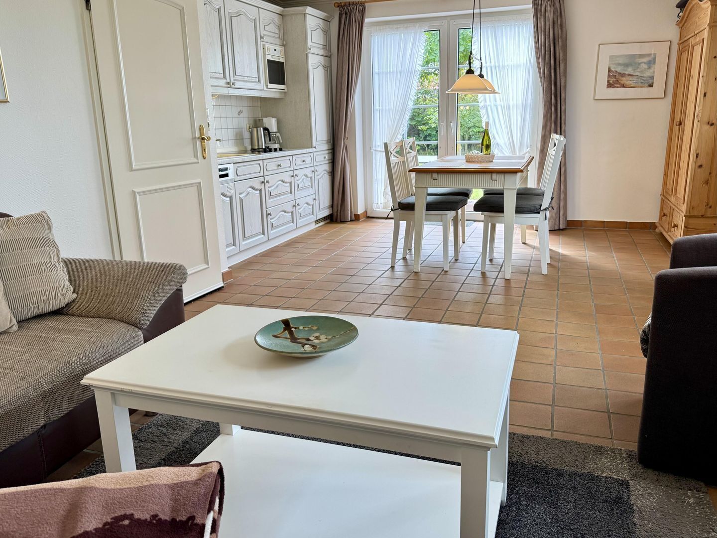 Uma sala de estar com uma mesa branca, um sofá e um espaço de jantar com uma mesa e cadeiras.