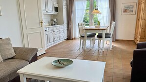 A living room with a white table, a sofa, and a dining area with a table and chairs. - Kampstraße, Apartment 2a - Cozy 2-room vacation apartment with a terrace in a quiet (Sylt)