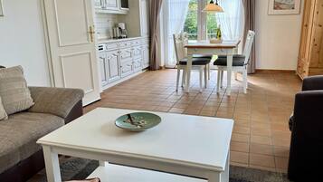 Uma sala de estar com uma mesa branca, um sofá e um espaço de jantar com uma mesa e cadeiras.