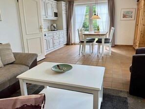 Ein Wohnzimmer mit einem weißen Tisch, einer Couch und einem Essbereich inklusive Tisch und Stühlen.