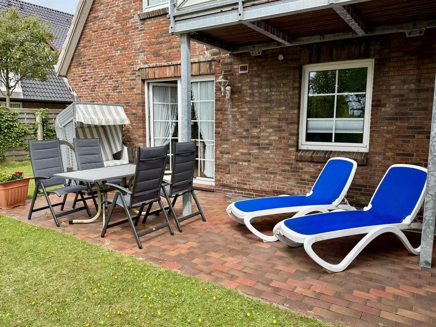 Eine Terrasse mit einer Ziegelmauer, einem Tisch mit Stühlen und zwei Liegestühlen.