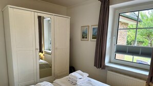A hotel room with two beds, a wardrobe, a window with blinds, and a radiator. - Kampstraße, Apartment 2a - Cozy 2-room vacation apartment with a terrace in a quiet (Sylt)