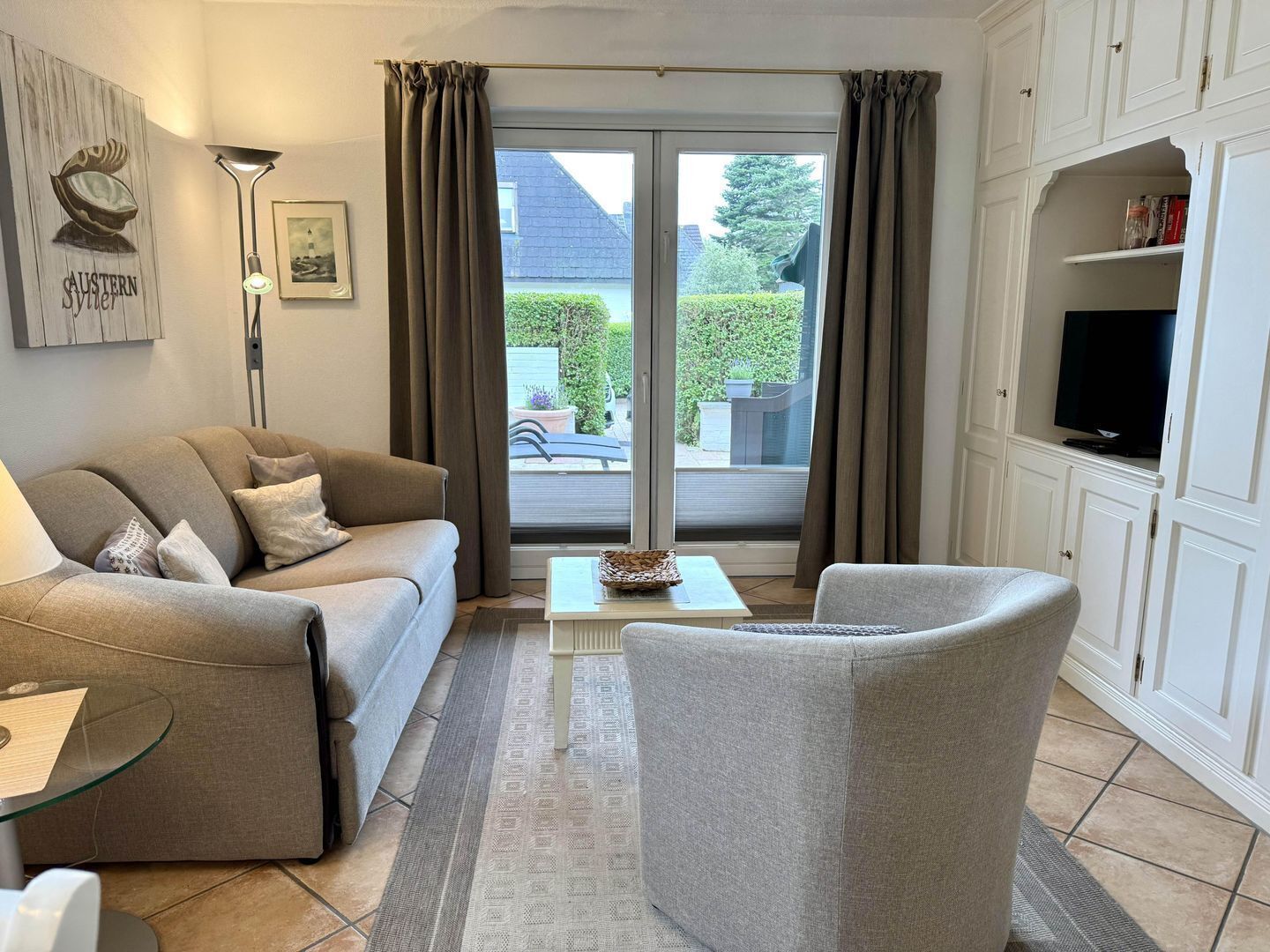 A living room with a sofa, armchair, coffee table, and a flat-screen TV on a cabinet.