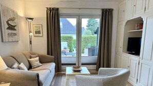 A living room with a sofa, armchair, coffee table, and a flat-screen TV on a cabinet. - Reiherweg, Apartment 1 - Beautiful 2-room vacation apartment with a terrace, quiet and (Sylt)