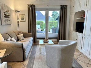 A living room with a sofa, armchair, coffee table, and a flat-screen TV on a cabinet. - Reiherweg, Apartment 1 - Beautiful 2-room vacation apartment with a terrace, quiet and (Sylt)