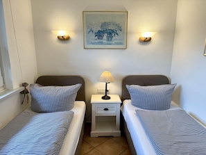 A twin room with two beds, each with striped bedding, a nightstand with a lamp, and a framed picture on the wall. - Reiherweg, Apartment 1 - Beautiful 2-room vacation apartment with a terrace, quiet and (Sylt)