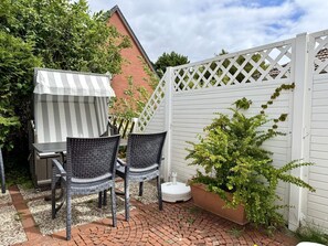 Eine Terrasse mit Tisch und Stühlen, ein weißes Gitter und ein Blumentopf.
