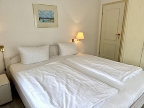A hotel room with a double bed, a bedside table, a lamp, a door, and a framed picture on the wall. - Süderstraße, Apartment 10 – Landhaus - Cozy 2-room vacation rental for 4 (Sylt)